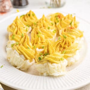 Closeup of a dozen deviled egg cupcakes topped with chopped chives and sprinkled with paprika on a white serving tray.