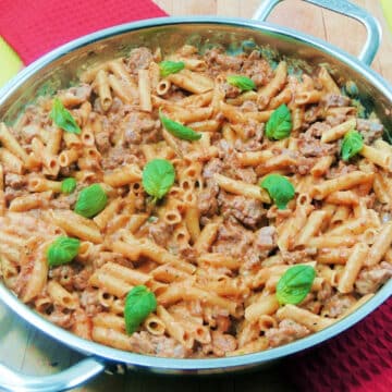 Closeup of Creamy Sun-Dried Tomato Pesto Pasta topped with fresh basil leaves in a silver skillet.