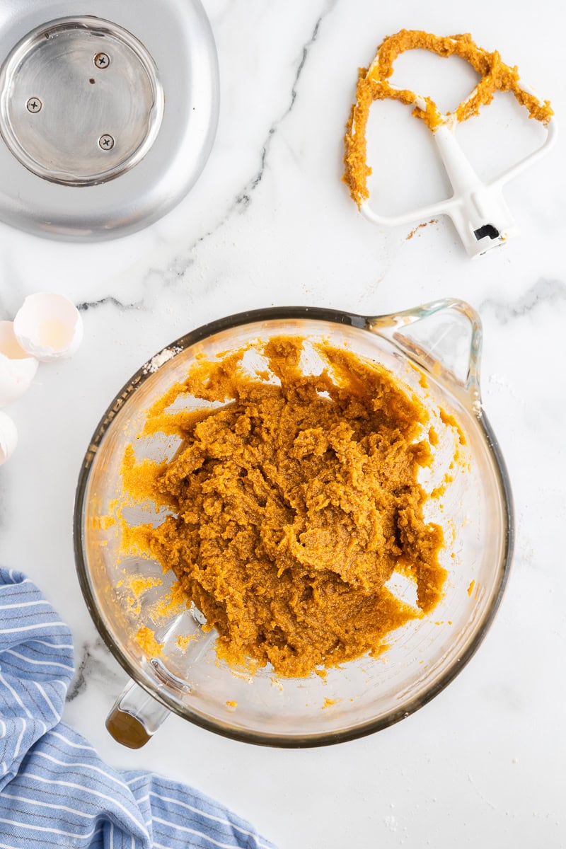 Overhead view of the pumpkin muffin batter combined in the glass bowl of a stand mixer.