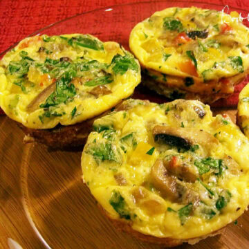 Three mini mixed vegetable frittatas on a glass plate that is on a wooden table with a red towek under the plate.