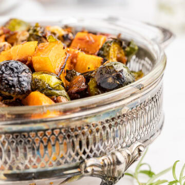 Closeup of keto maple roasted brussels sprouts and butternut squash in a glass serving dish with silver handles.