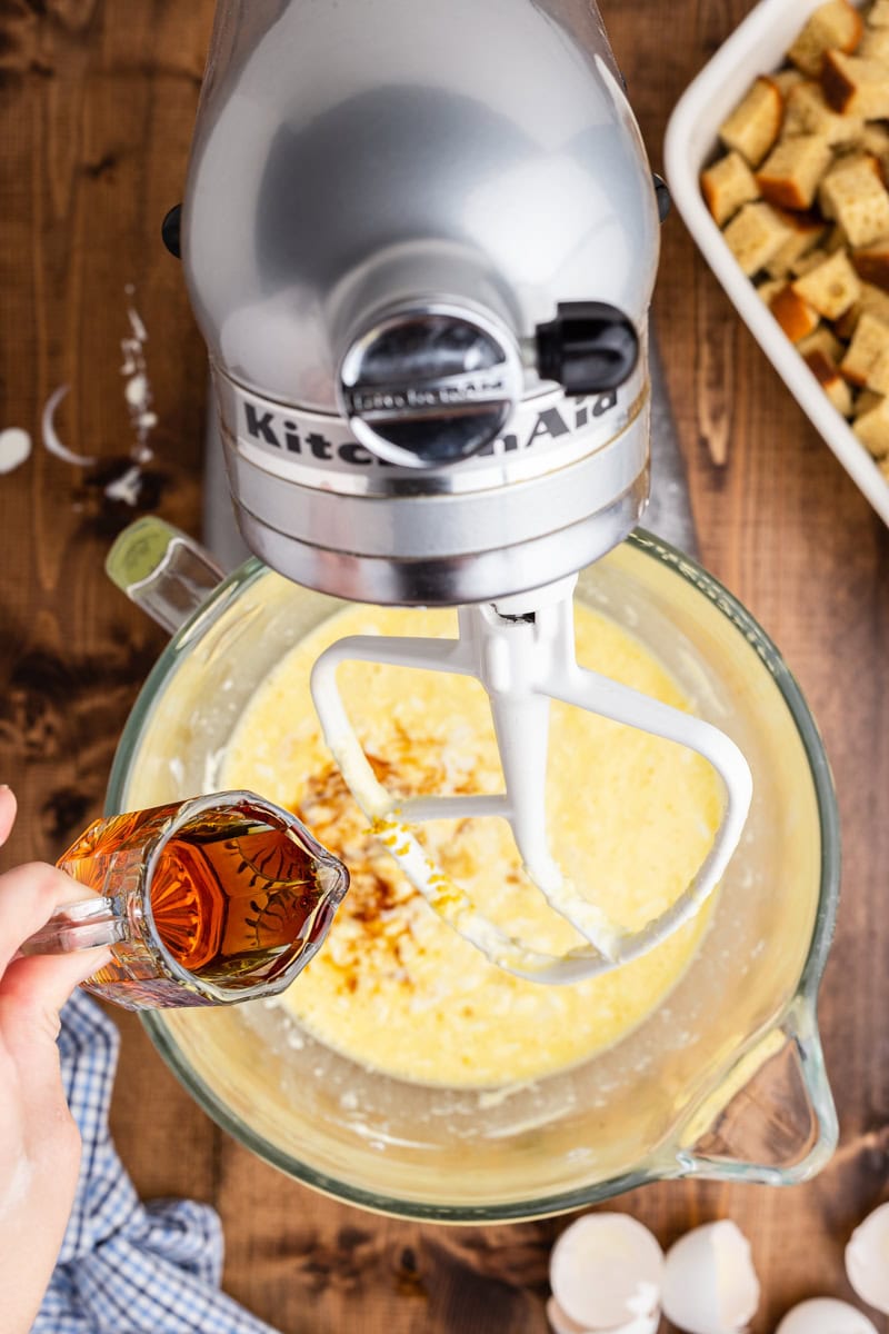 Overhead view of a stand mixer with cream cheese, eggs, almond milk, heavy cream, maple syrup, vanilla, and lemon zest in the bowl.