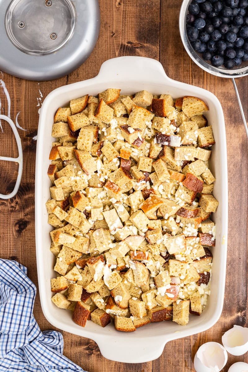 Overhead view of a 9 x 13 baking dish on a wooden table. There are keto bread cubes topped with the egg custard mixer.