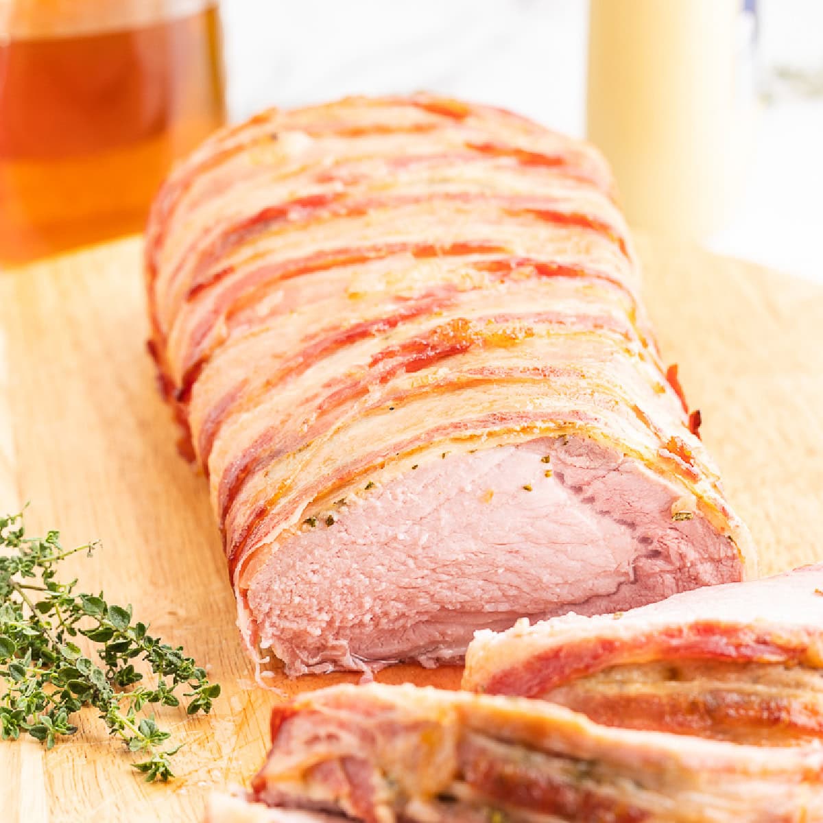 Closeup of a sugar-free keto bacon wrapped honey mustard pork loin on a wooden cutting board with several slices cut.