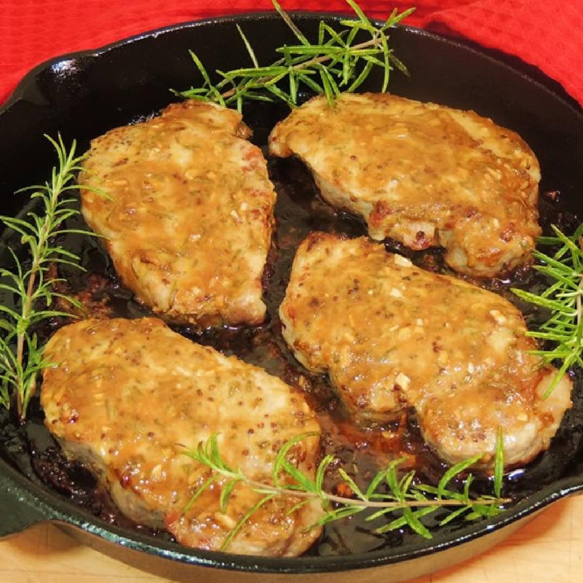 Four keto honey mustard pork chops in a cast iron skillet with sprigs of fresh rosemary.