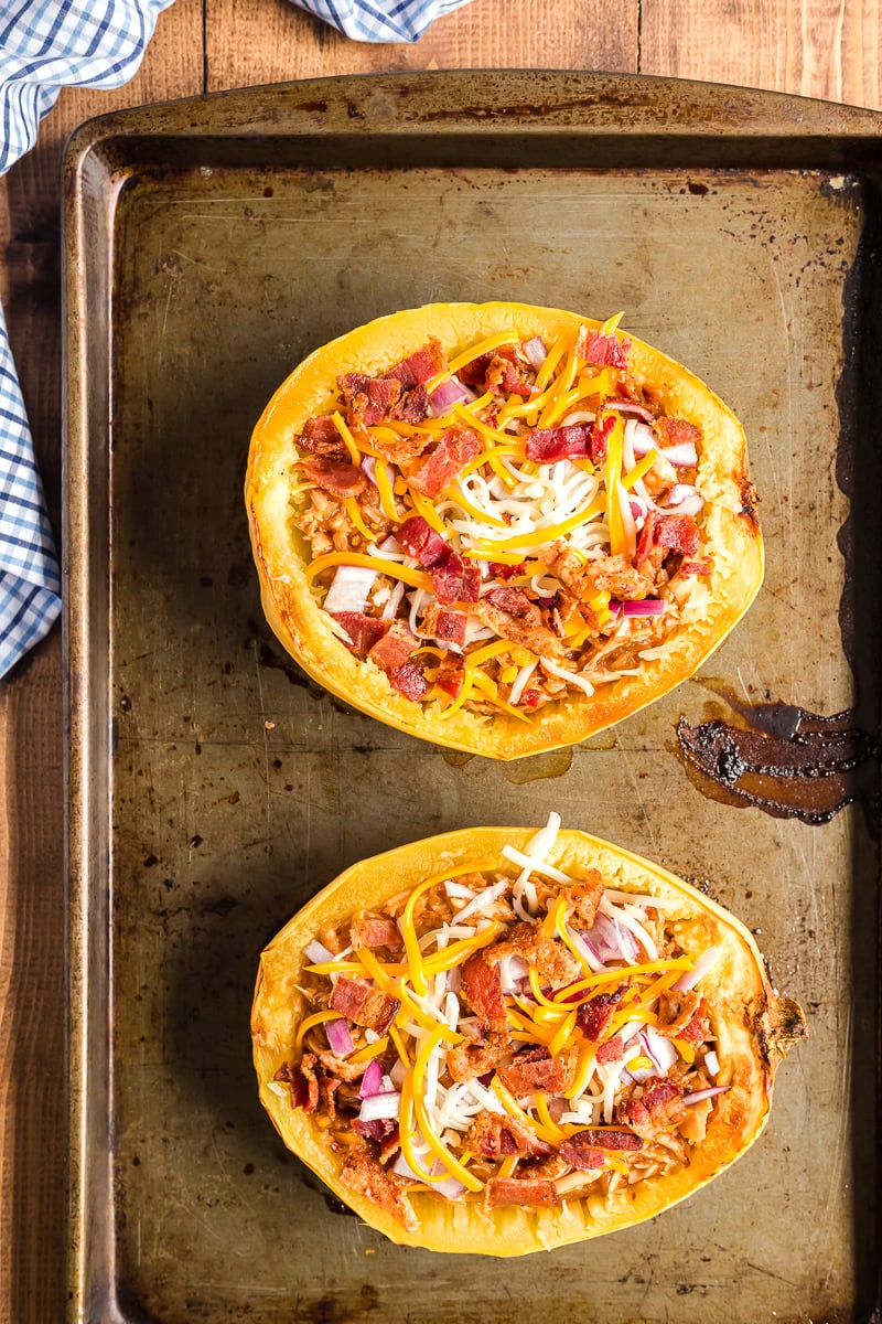 Two spaghetti squash halves stuffed with shredded BBQ chicken and cheese on a baking sheet.