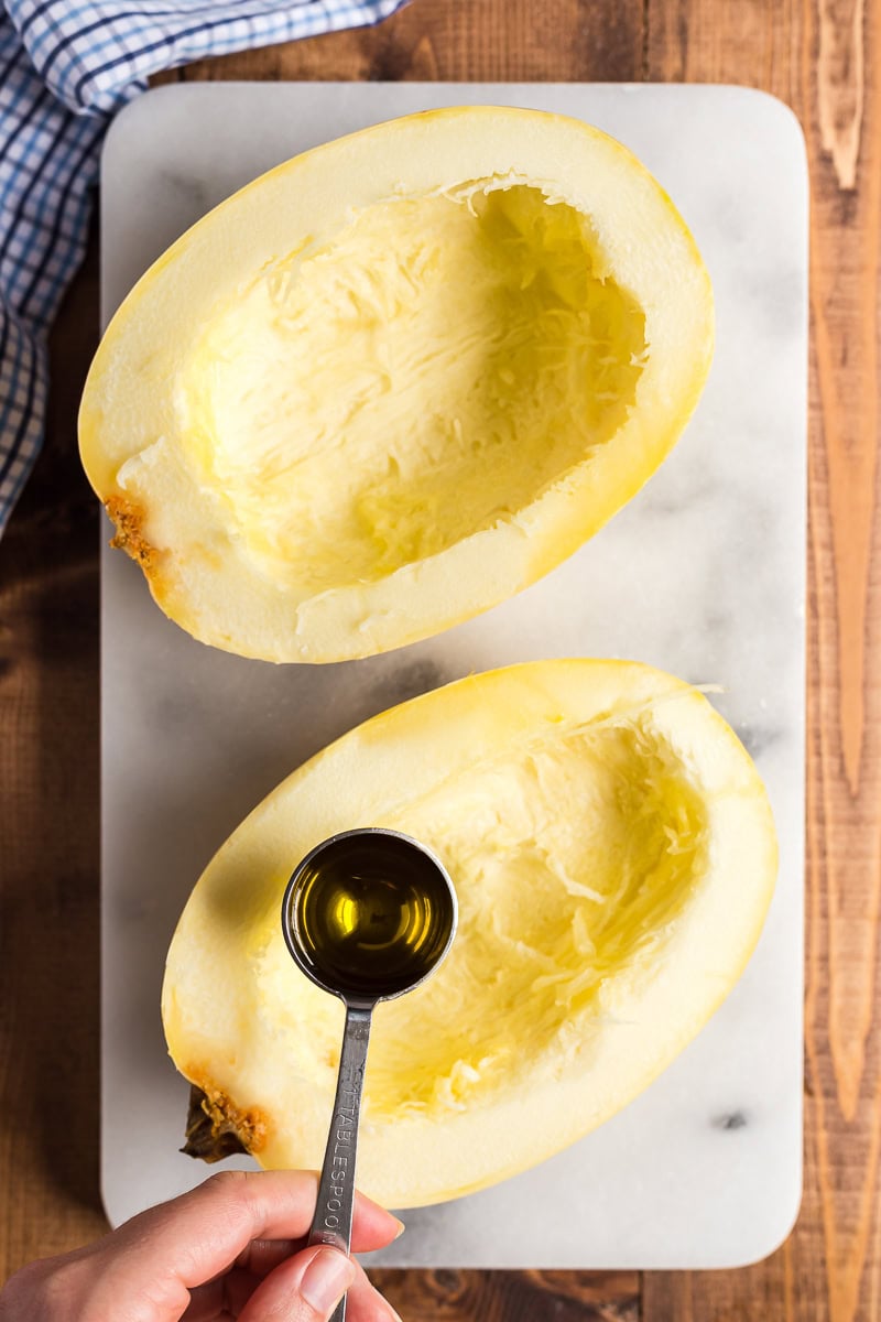 Overhead view of a spaghetti squash cut in half being brushed with olive oil before roasting.