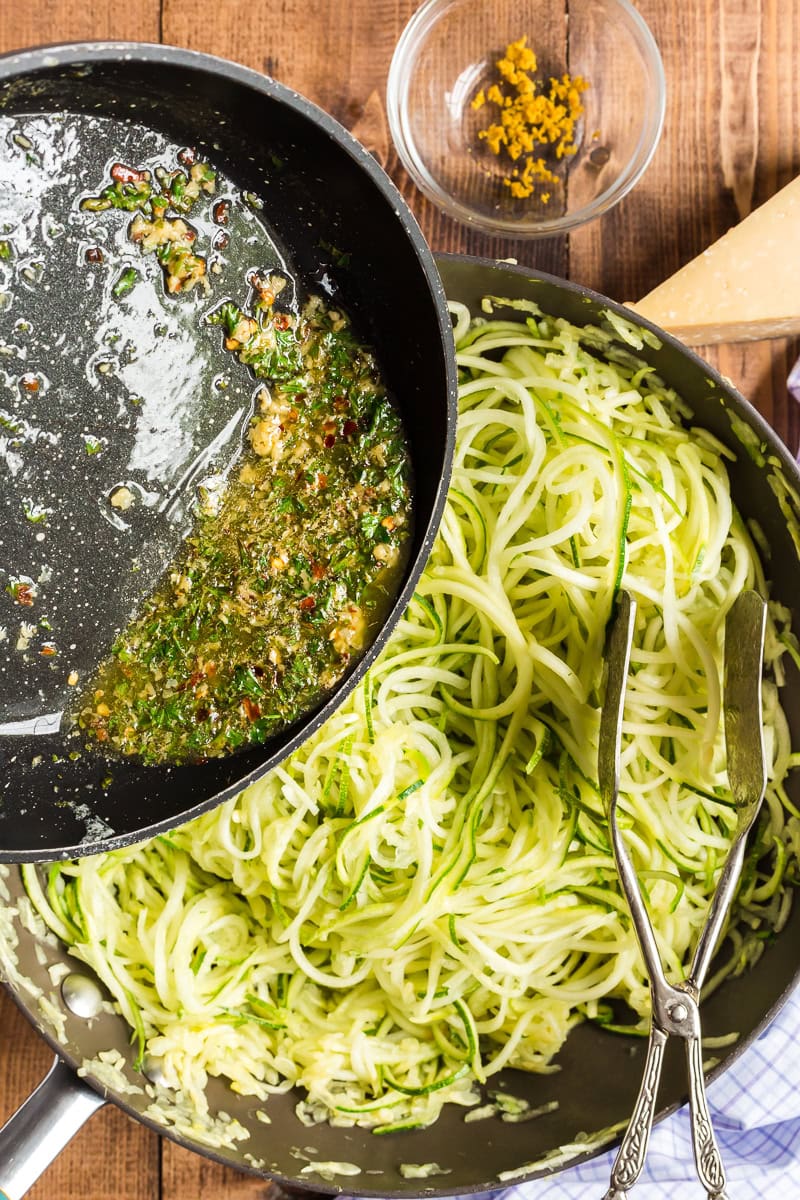 Lemon garlic butter sauce being added to zucchini noodles in a large skillet.