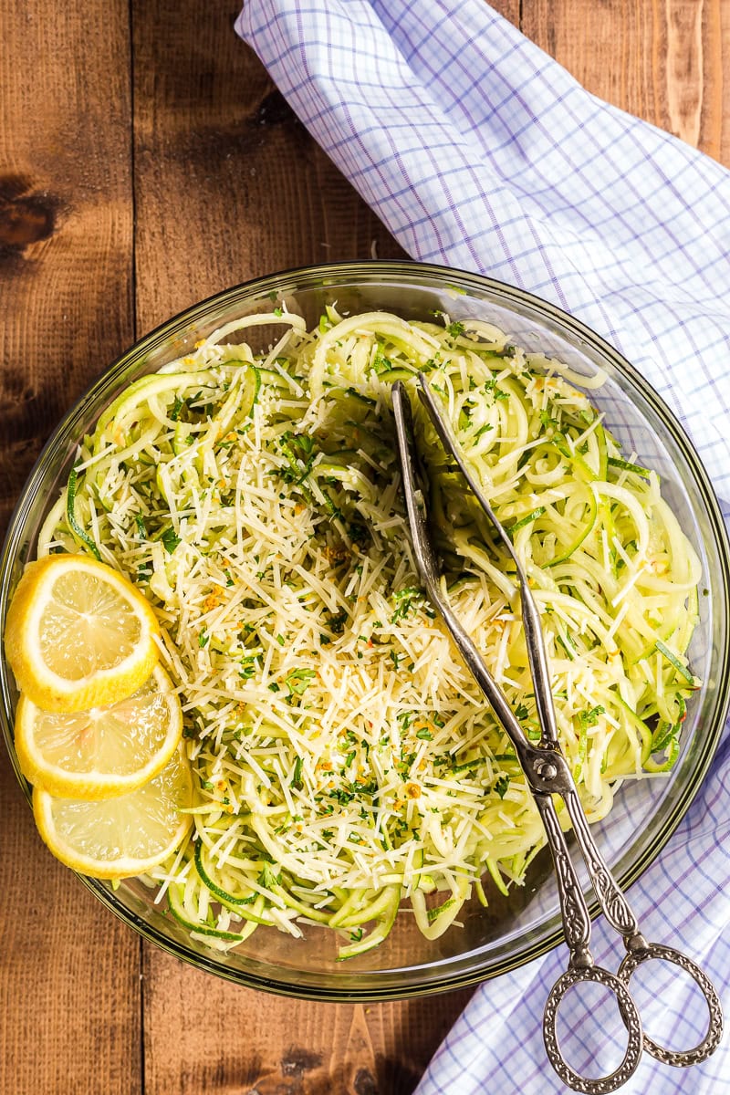 Overhead view of lemon garlic zucchini noodles in a large skillet garnished with lemon slices, parmesan cheese, and fresh chopped parsley.