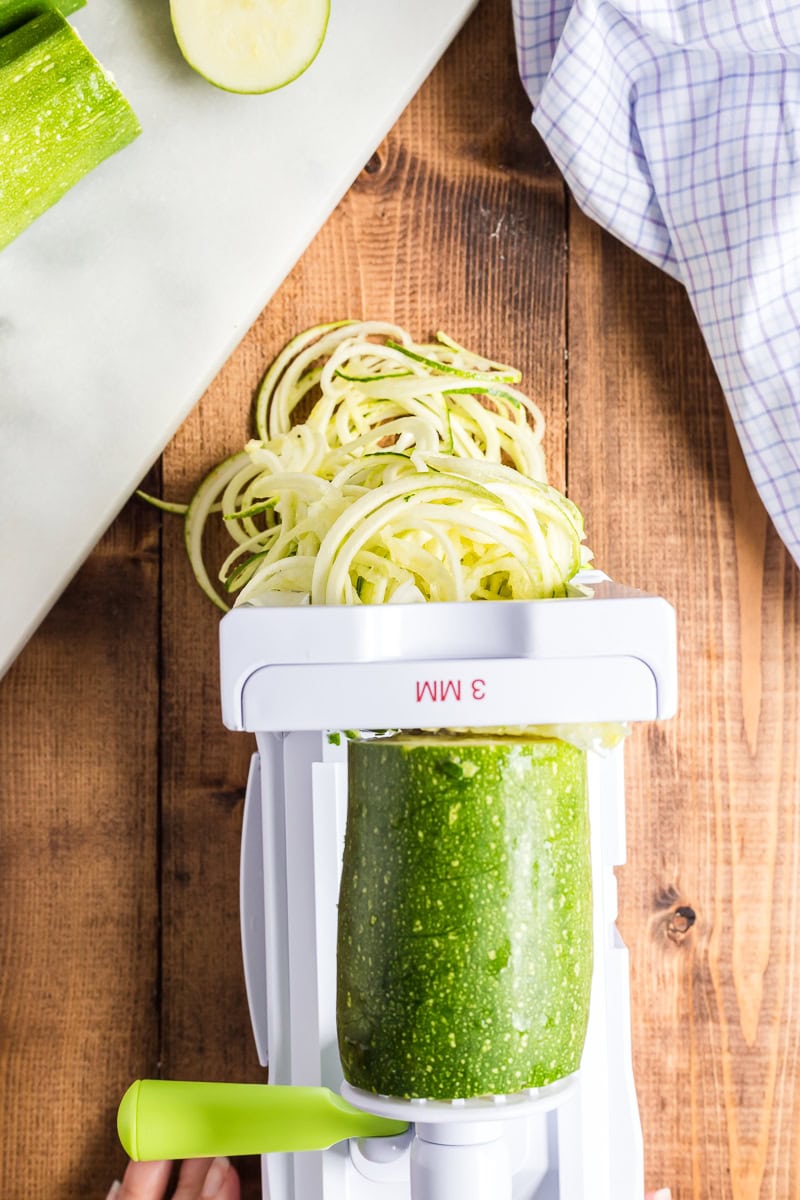 Overhead view of a zucchini being spiralized into noodles on a wooden table.