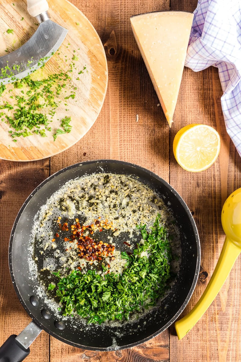 Overhead view of butter, garlic, lemon juice, parsley, and red pepper flakes in a large cast iron skillet.