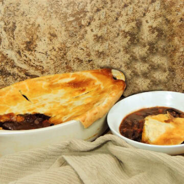 Beef and mushroom pot pie in a white 2 quart baking dish with a white bowl that holds a serving sitting next to it.