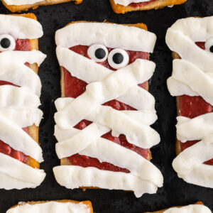 Closeup of several keto cheesecake mummy cookies on a black plate.