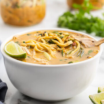 A white bowl full of spicy chicken noodle soup on a white counter.