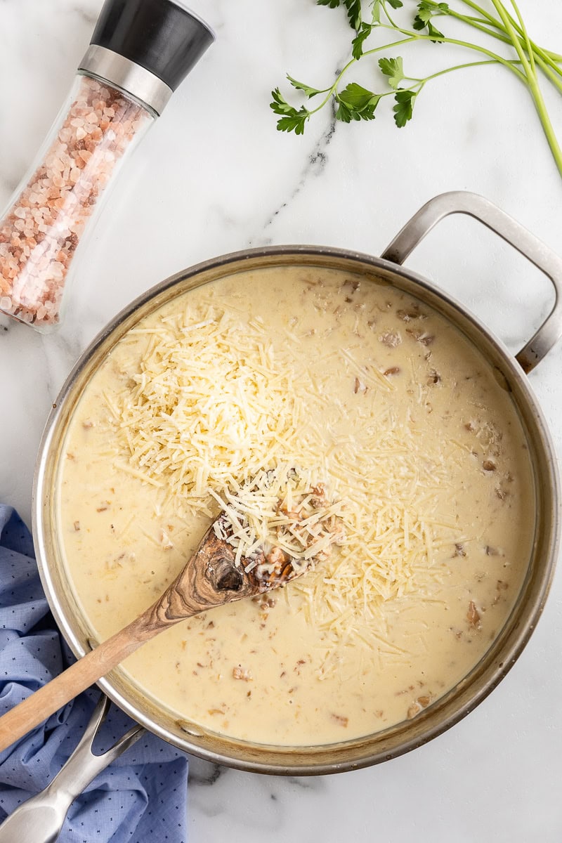 Overhead view of a large skillet containing shallots, garlic, baby clams, white wine, heavy cream, and parmesan cheese.