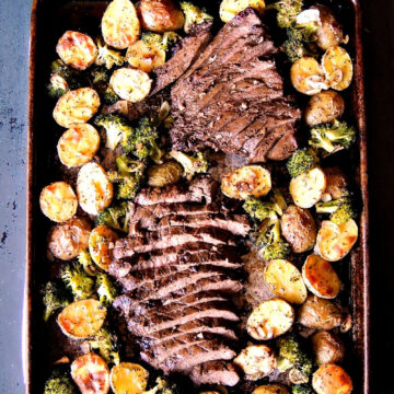 Overhead view of a sliced flank steak on a sheet pan with roasted potatoes and broccoli.