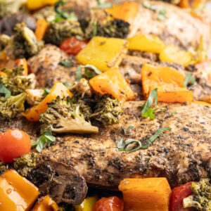 Several balsamic glazed chicken breasts on a sheet pan with low-carb vegetables.