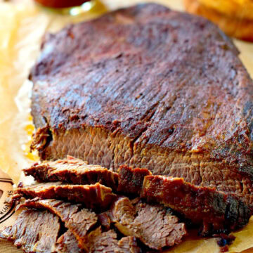 Closeup of a slow cooker smoked brisket on a wooden cutting board with a few slices carved from it.
