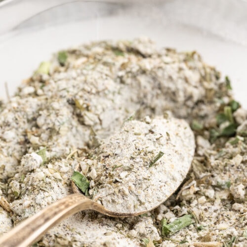 Closeup of homemade ranch dressing mix in a glass bowl with a silver spoon.