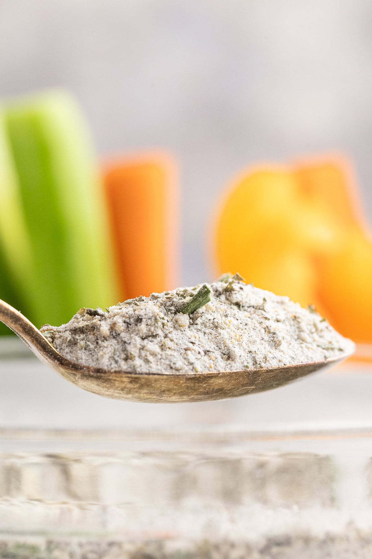 Close-up of a spoonfull of hoemmade ranch dressing mix with fresh vegetables in the background.