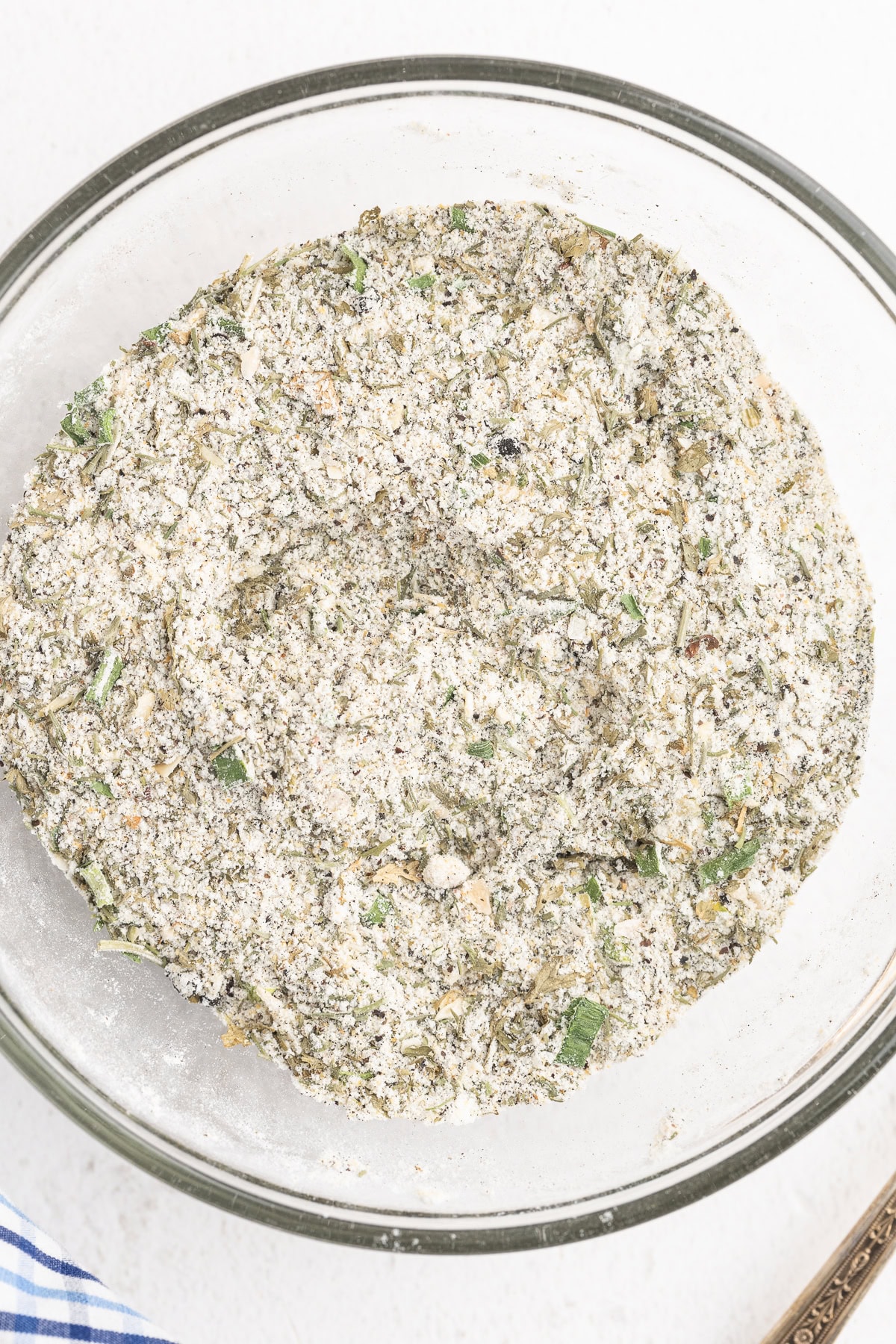 Closeup overhead view of homemade ranch seasoning mix in a small glass bowl on a white counter.