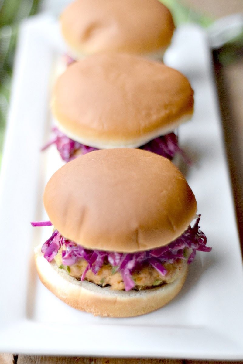 several salmon sliders topped with lemon dill slaw on a white serving tray.