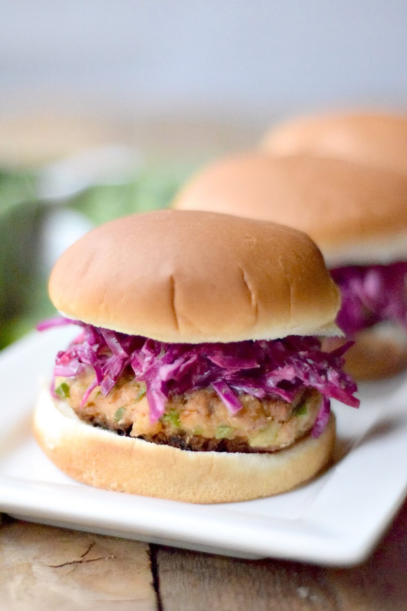 Close up side view of a crispy salmon slider topped with lemon dill slaw on a white serving tray.
