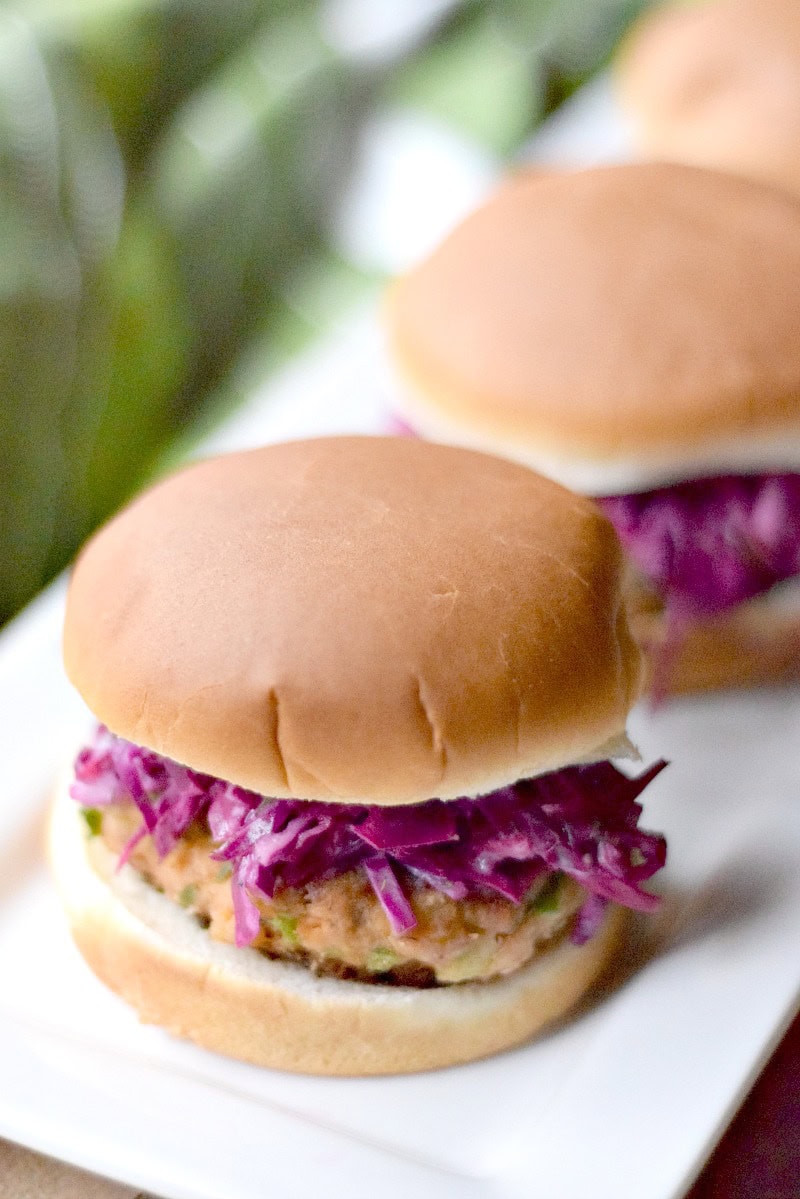 Salmon sliders topped with lemon dill slaw on a white serving platter.