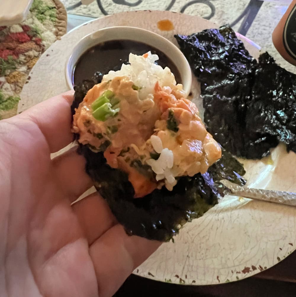 Overhead view of a white hand holding a seaweed snack with a scoop of the sushi bake on it.