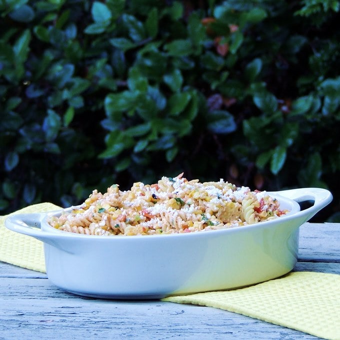 A sideview of the Mexican Street Corn Pasta Salad in a white serving dish with greenery in the background.