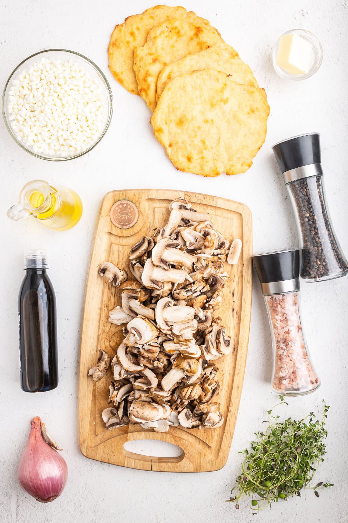 All of the ingredients needed to make low-carb mushroom goat cheese flatbreads on a white marble counter.