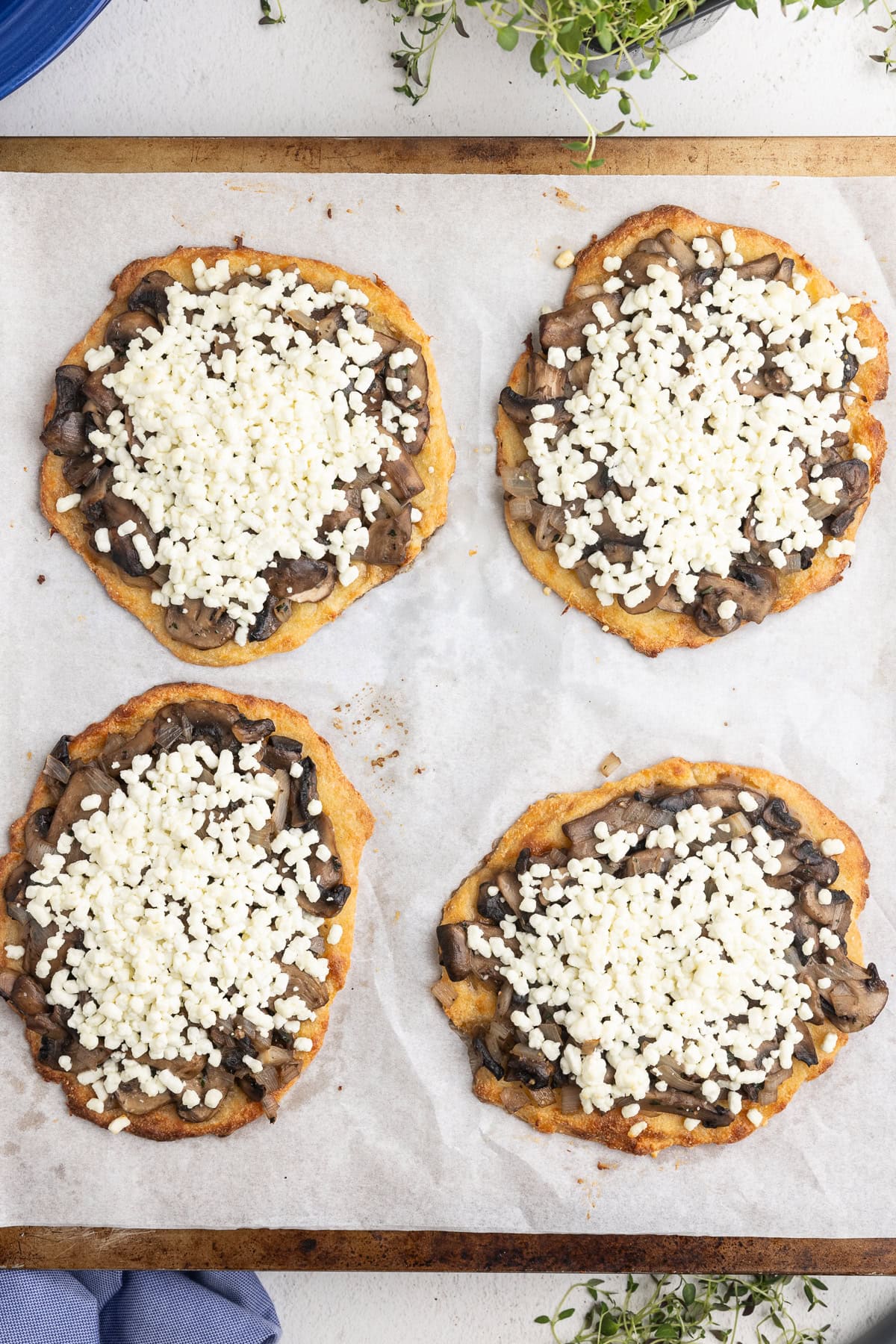 Overhead view of the assembled low-carb mushroom goat cheese flatbreads on a parchment lined baking sheet.