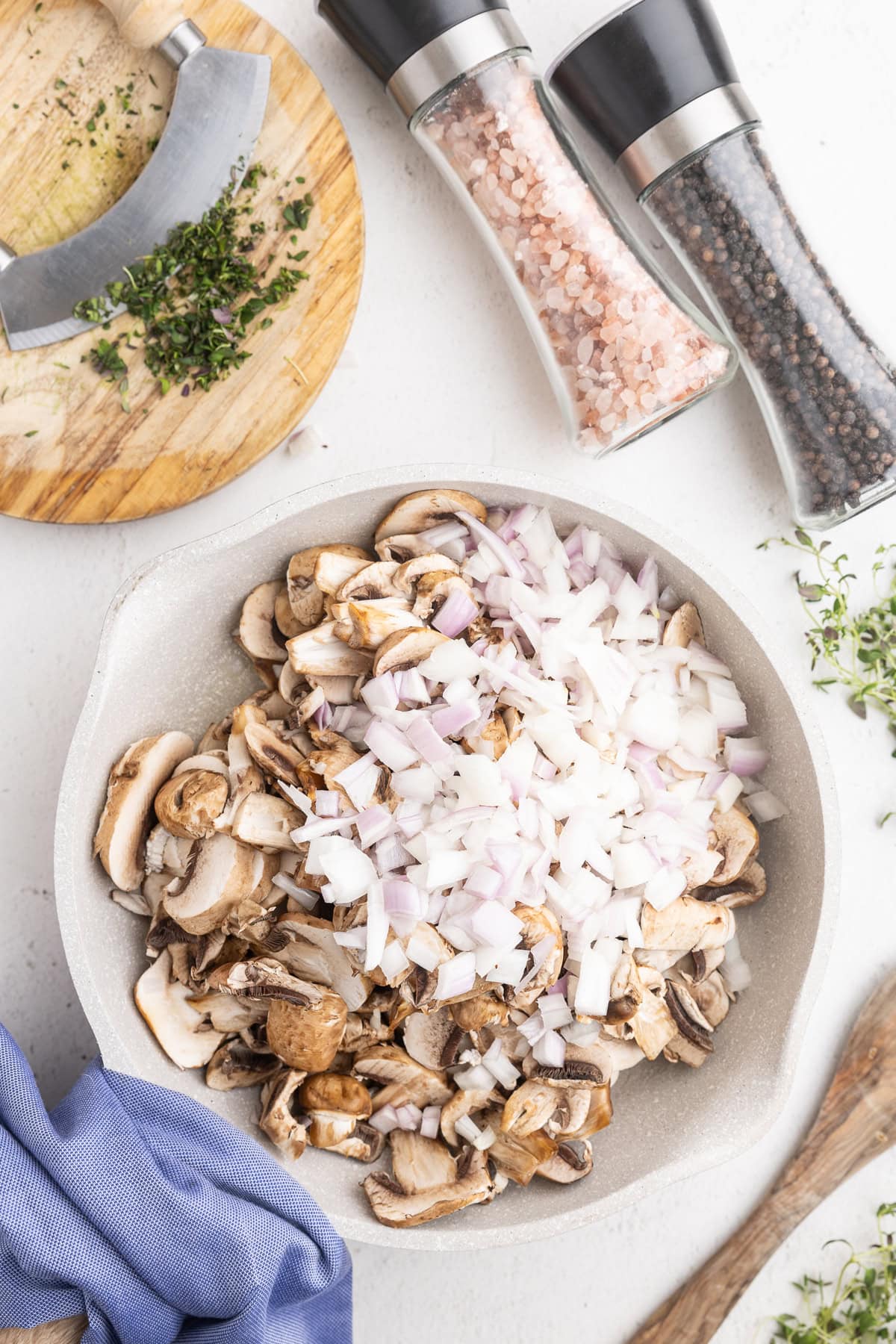 Sliced mushrooms and onions sauteing in a white skillet.