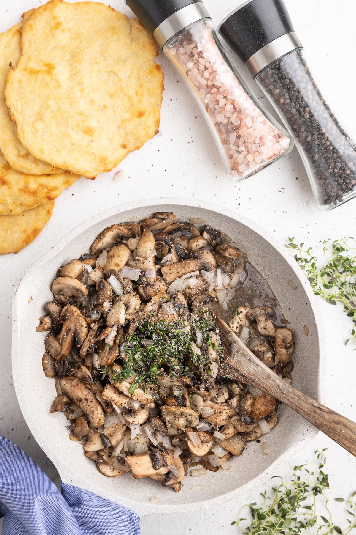 Sauted mushrooms and onions in a white skillet topped with herbs and seasoning.