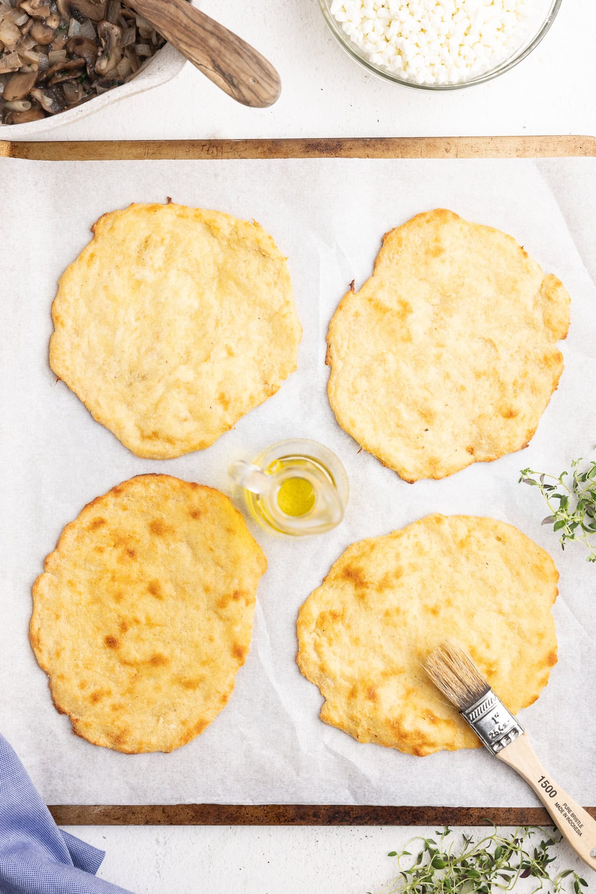 Low-carb flatbreads brushed being brushed with olive oil on a parchment lined baking sheet.