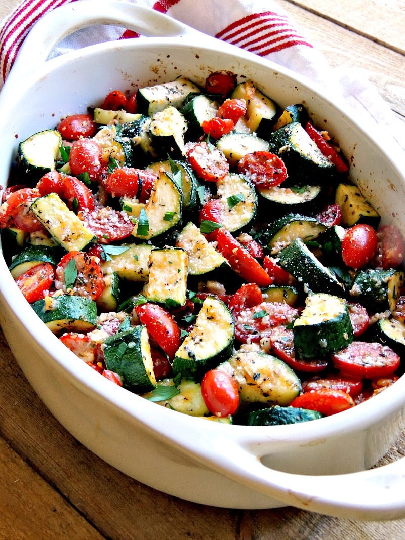 Overhead view of deliciously roasted garlic parmesan tomatoes and zucchini in a white baking dish.