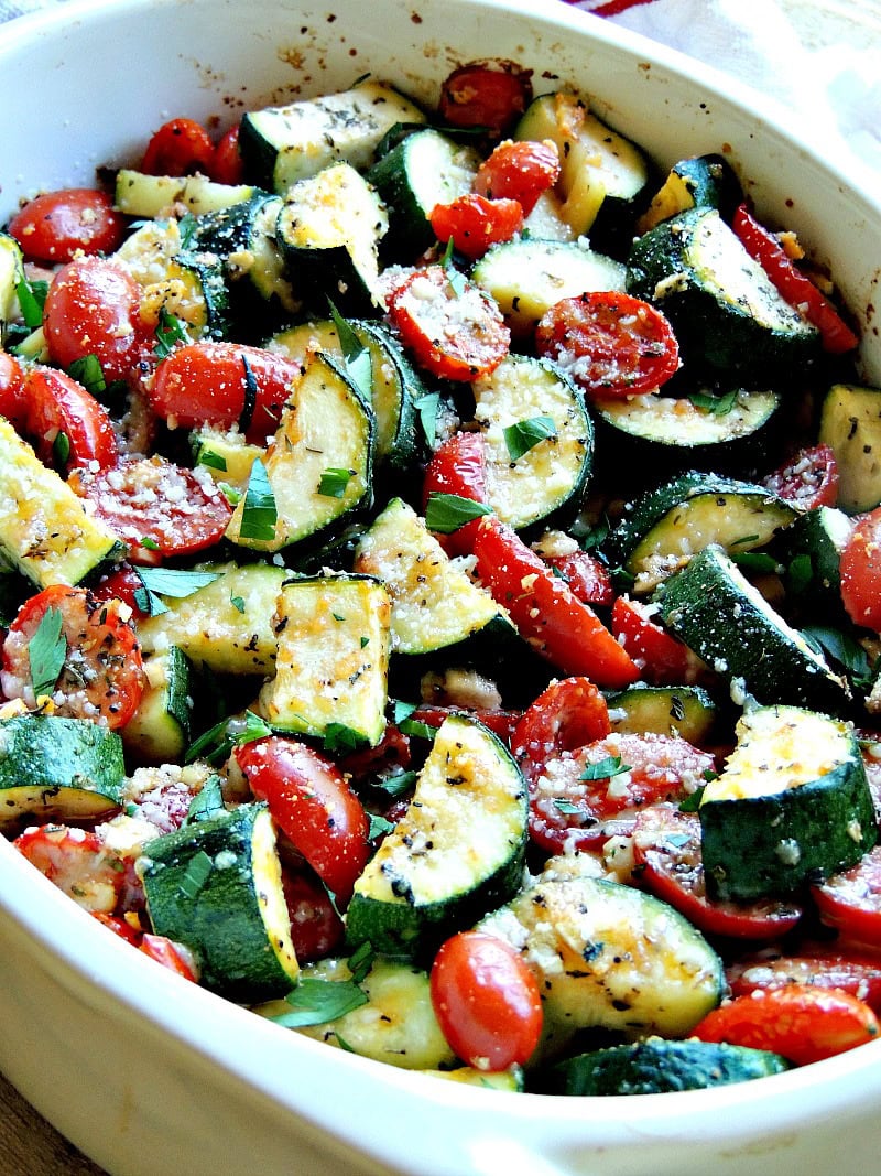 Close up view of garlic parmesan baked zucchini and tomatoes in a white baking dish.
