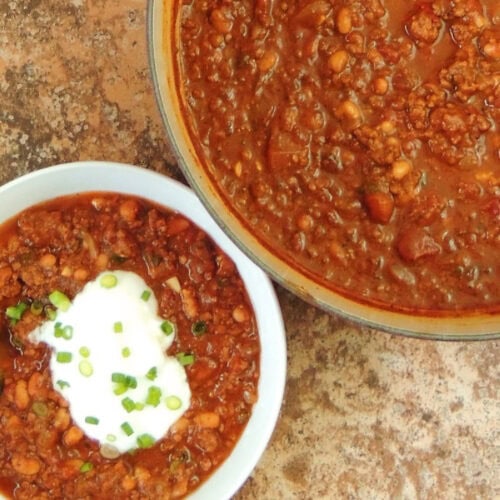 Closeup of a large pot full of pumpkin chili next to a bowl of the chili topped with sour cream.